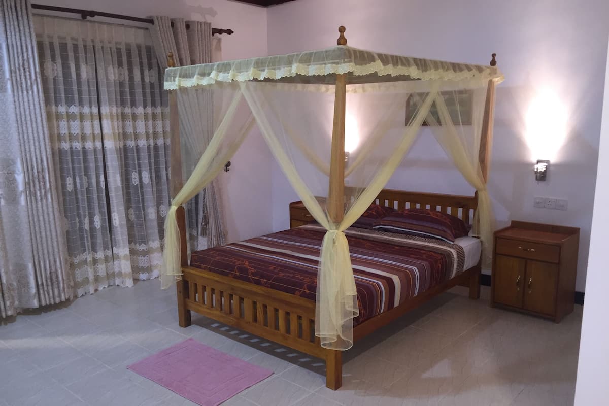 A four-poster bed with a canopy, a wooden nightstand, and a pink rug on a tiled floor.