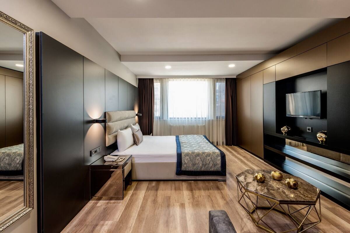 A modern hotel room with a large bed, a TV, a bedside table, and a mirror.