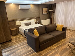 Relax in a spacious room with a large bed, sofa, and nightstand, featuring a wall-mounted air conditioner and a framed painting.