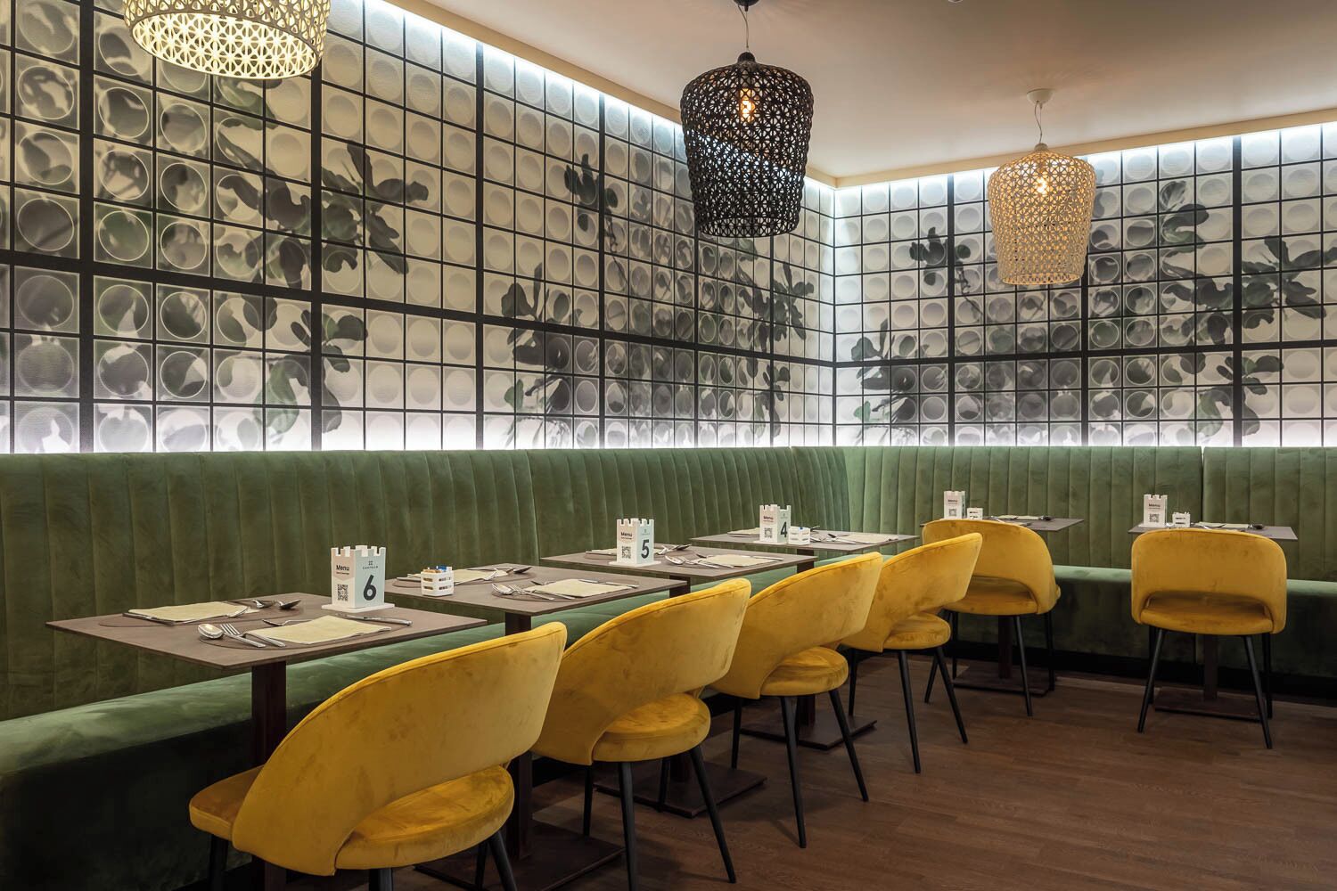 A restaurant interior with green cushioned booths, yellow chairs, and a patterned wall with circular designs.