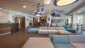 A modern hotel lobby with a reception desk, seating areas, and a bar. - Hotel Castello (L'Aquila)