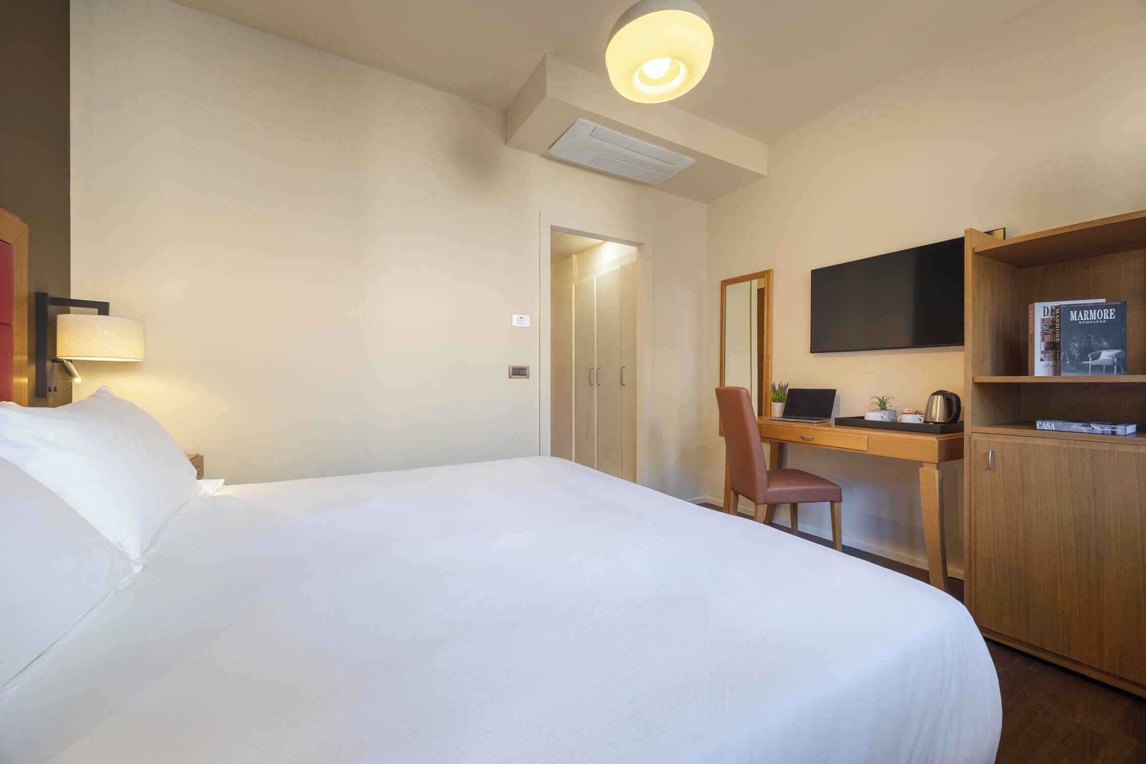 A hotel room with a bed, desk, chair, television, and a bookshelf.