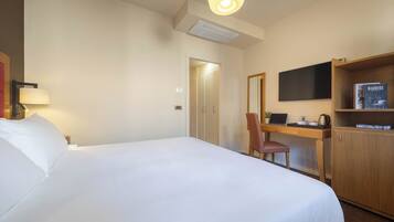 A hotel room with a bed, desk, chair, television, and a bookshelf.