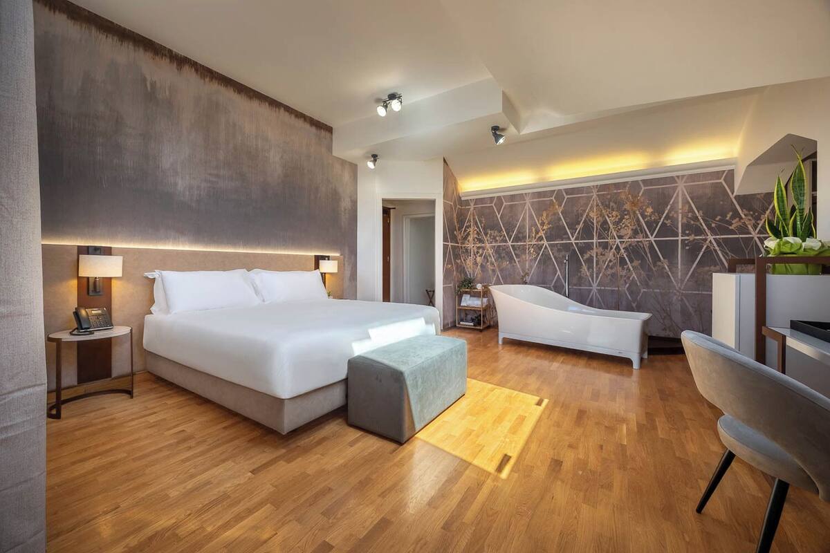 Una habitación de hotel moderna con una cama grande, una bañera, un escritorio y una pared con diseños geométricos.