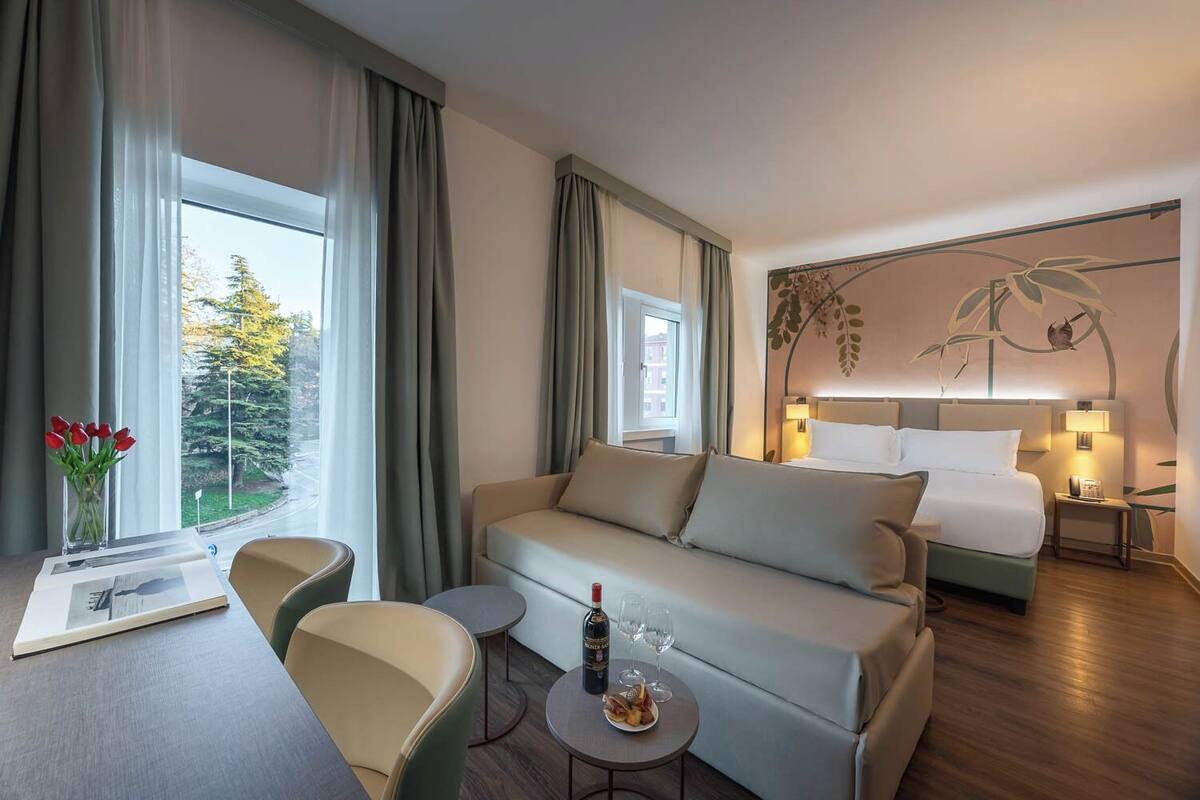 Una habitación de hotel con cama, sofá, mesa de comedor y una mesita con una botella y vasos.