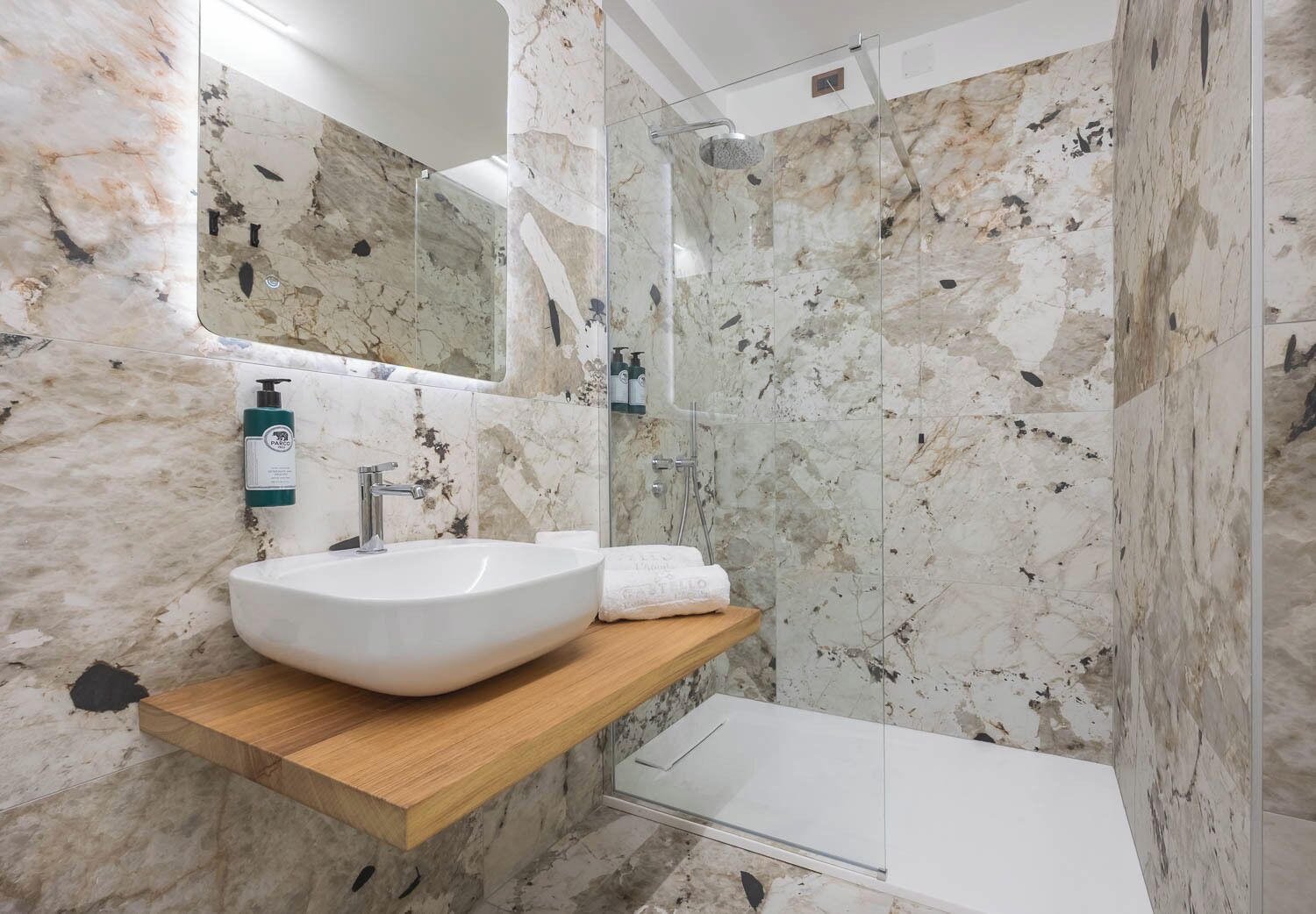 A bathroom with a marble sink, a wooden shelf, a glass shower enclosure, and a large mirror.