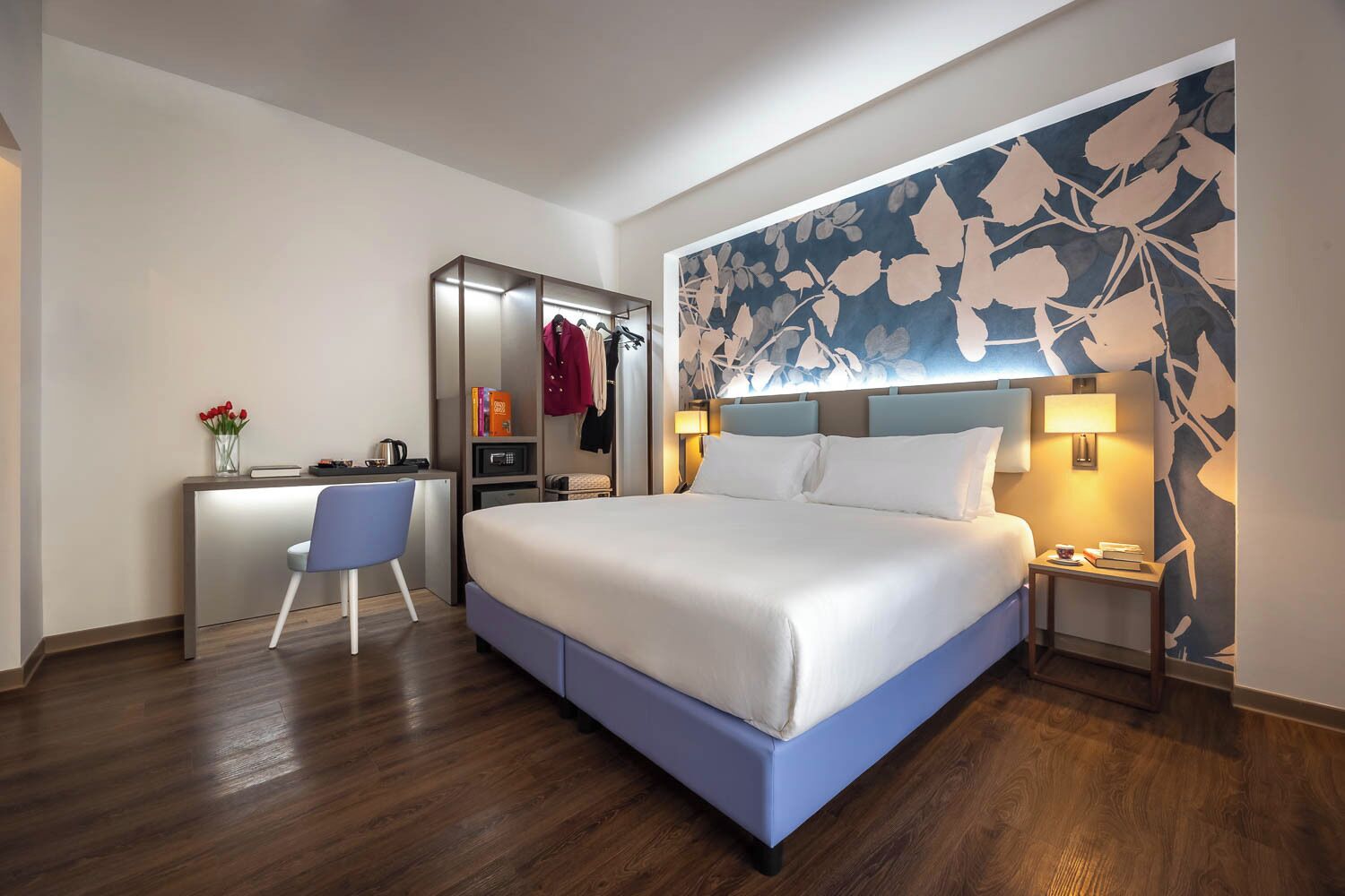 Habitación de hotel con cama, escritorio, silla y un amplio mural floral.