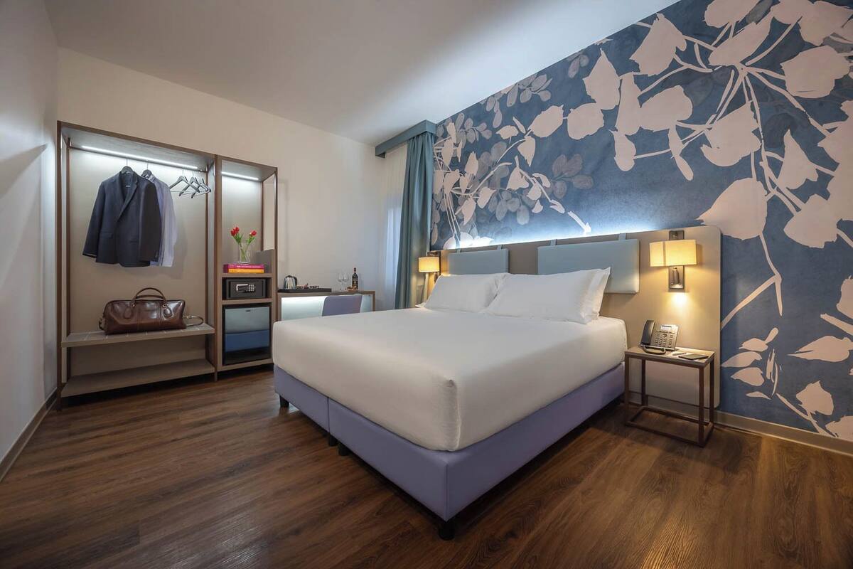 Una habitación de hotel con cama, escritorio, armario y papel tapiz floral.