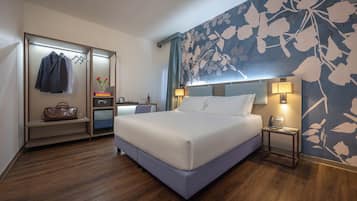 A hotel room with a bed, a desk, a wardrobe, and a floral wall.