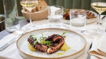 A dining table with plates of food, glasses of white wine, and a bowl of bread.