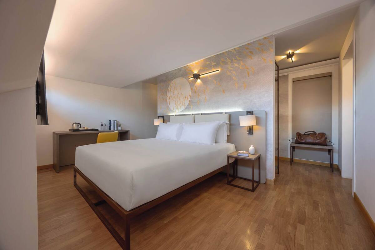 Una habitación de hotel con una cama grande, un escritorio, una silla, un banco y un perchero.