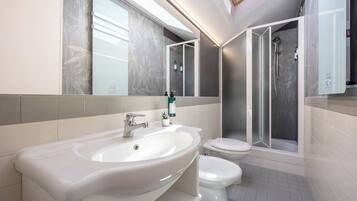 A modern bathroom with a skylight, a sink, two toilets, and a shower enclosure.