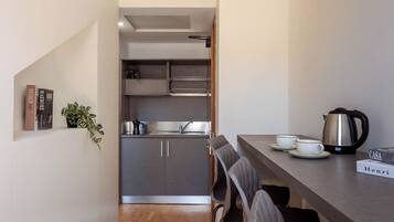 A compact kitchen with a sink, cabinets, and a coffee maker. There are chairs and a table with a book and a kettle.