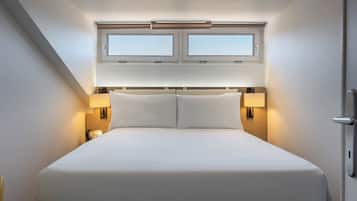A hotel room with a large bed, two bedside lamps, a window with blinds, and a door.