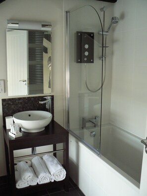 A modern bathroom with a glass-enclosed shower, a white sink, and neatly rolled towels on a shelf. - Cape Cornwall golf & Leisure (Penzance)