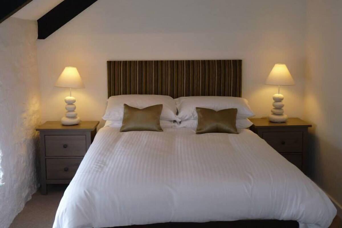 A neatly made bed with a striped headboard, two bedside tables with lamps, and a small drawer.