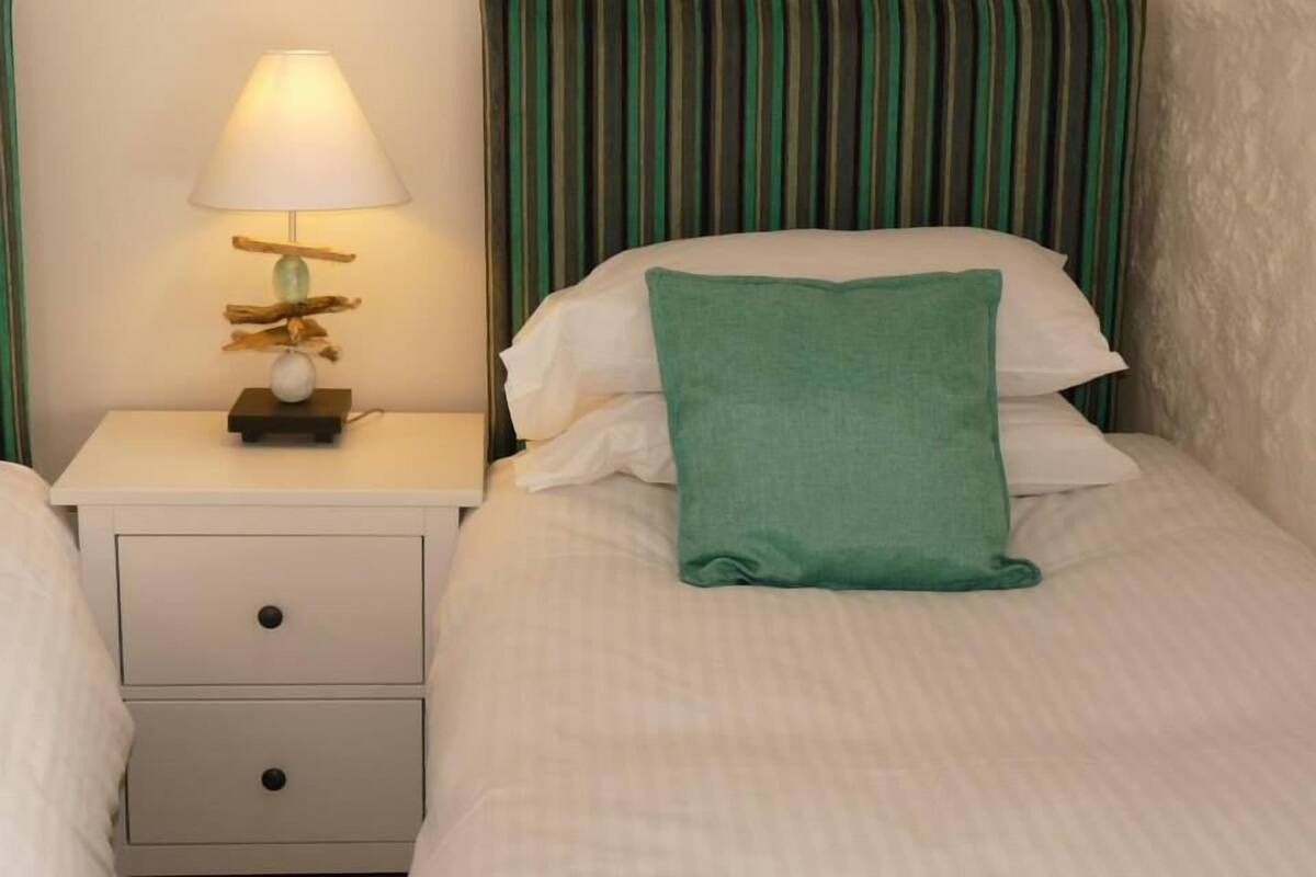 A neatly made bed with a green pillow and a white pillow, a bedside table with a lamp, and a striped headboard.