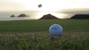 A golf ball on a grassy field with a flag in the background and a body of water. - Cape Cornwall golf & Leisure (Cornwall)