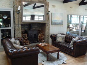 A cozy living room with a stone fireplace, leather sofas, and a wooden coffee table. - Cape Cornwall golf & Leisure (Cornwall)