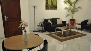A modern living room with a black sofa, a wooden coffee table, and a potted plant. - Le Suites Serviced Apartments (Accra)