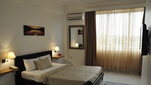A hotel room with a bed, bedside lamps, a mounted TV, a window with curtains, and a painting on the wall. - Le Suites Serviced Apartments (Accra)
