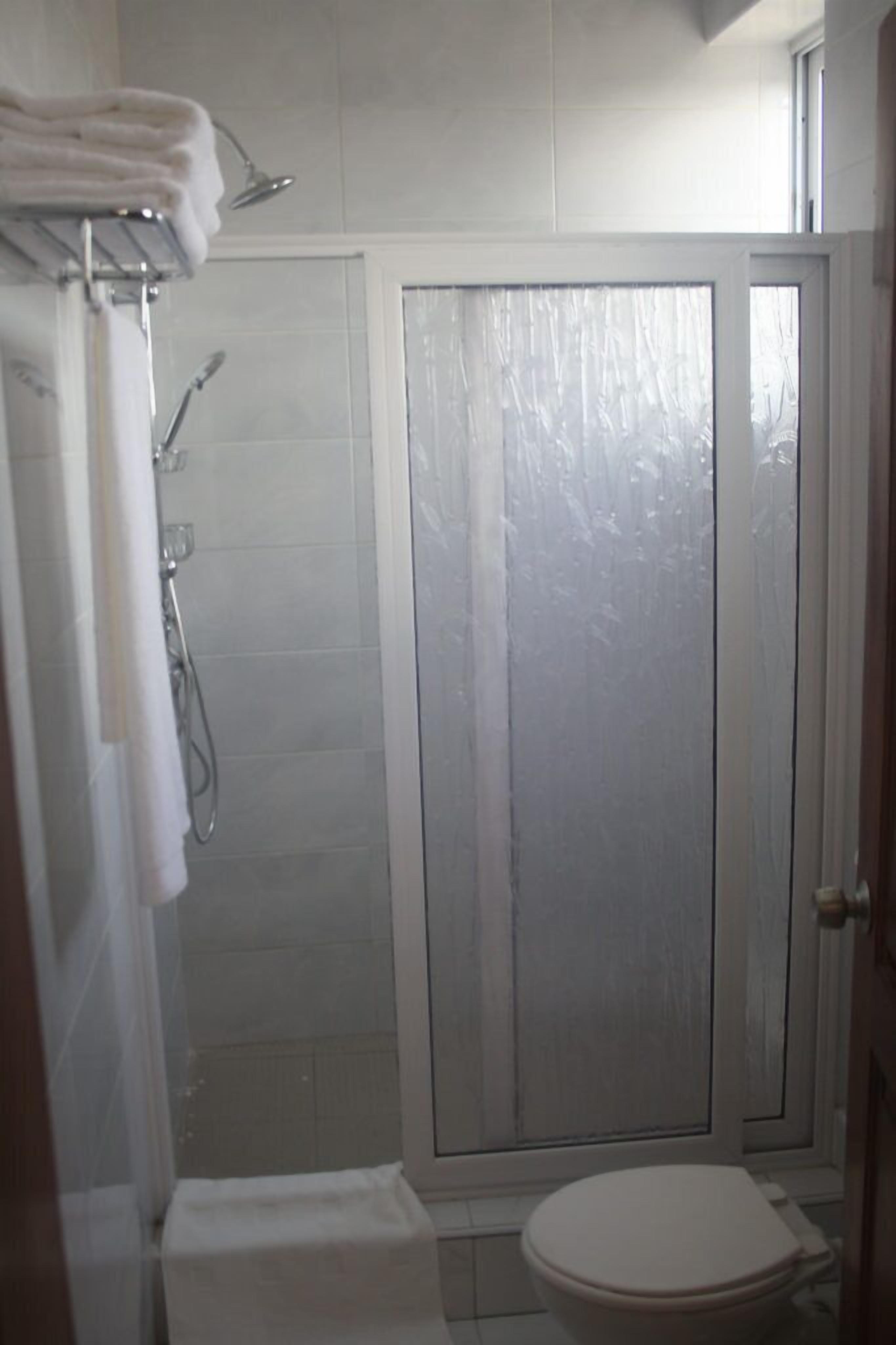 A bathroom with a shower, toilet, and a glass door.