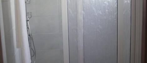 A bathroom with a shower, toilet, and a glass door.