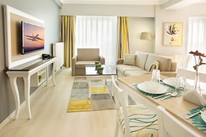A modern living room with a flat-screen TV, a sofa, a coffee table, and a dining area with a table set for two.