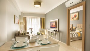 Habitación de hotel moderna con zona de comedor, cama con colcha estampada y un cuadro en la pared.