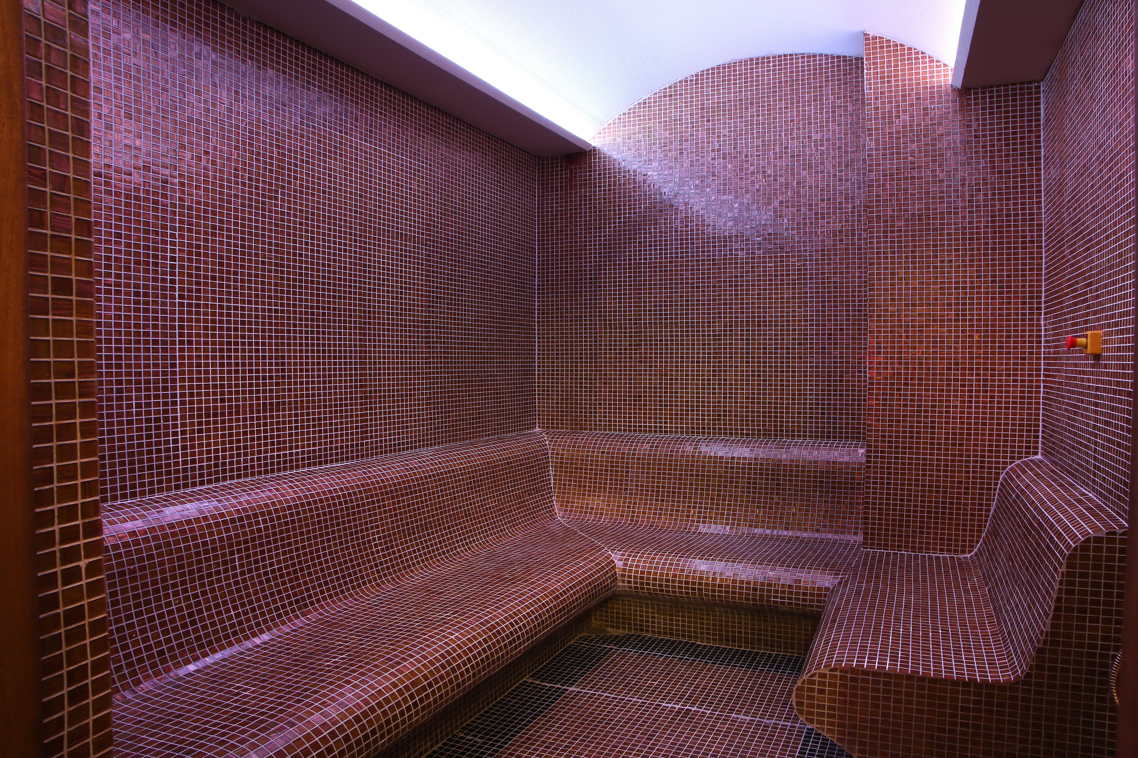 A tiled sauna with a bench and a small table, featuring a sloped ceiling and a skylight.