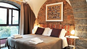 A bedroom with a stone wall, a bed with pillows, a bedside table, and a window with curtains. - La Corte dei Limoni (Acireale)