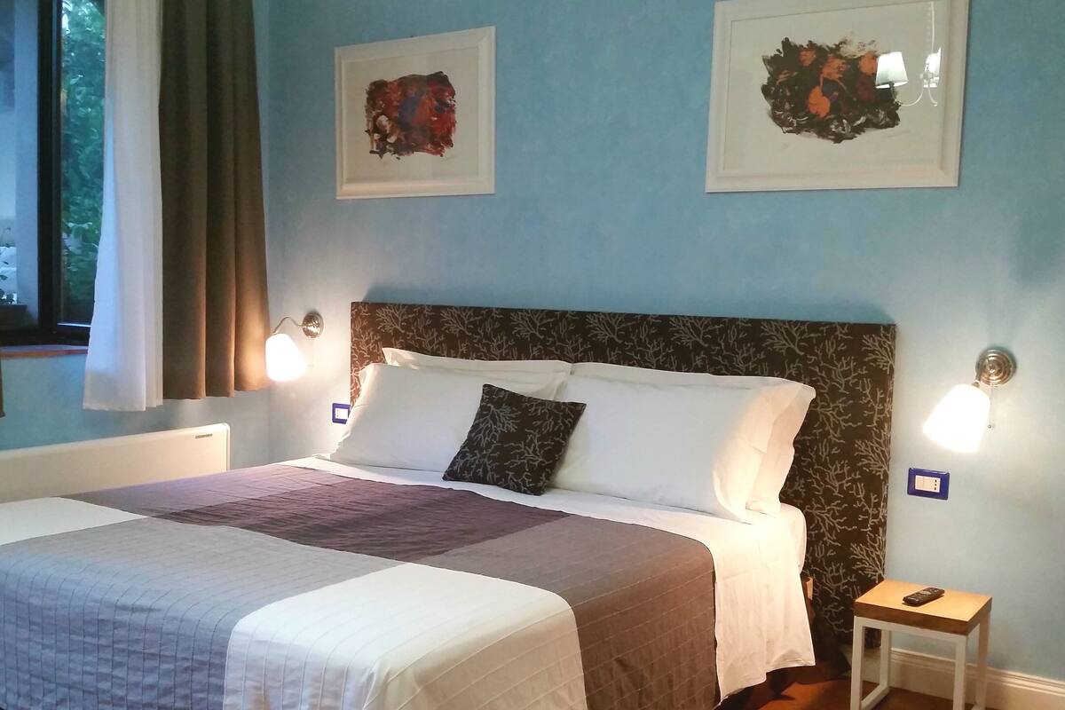 A neatly made bed with a patterned bedspread, a headboard with a leaf pattern, and two wall-mounted light fixtures.