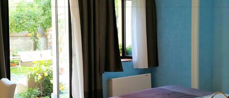 Un dormitorio con cama, una silla, un ventanal con cortinas y vistas al exterior.