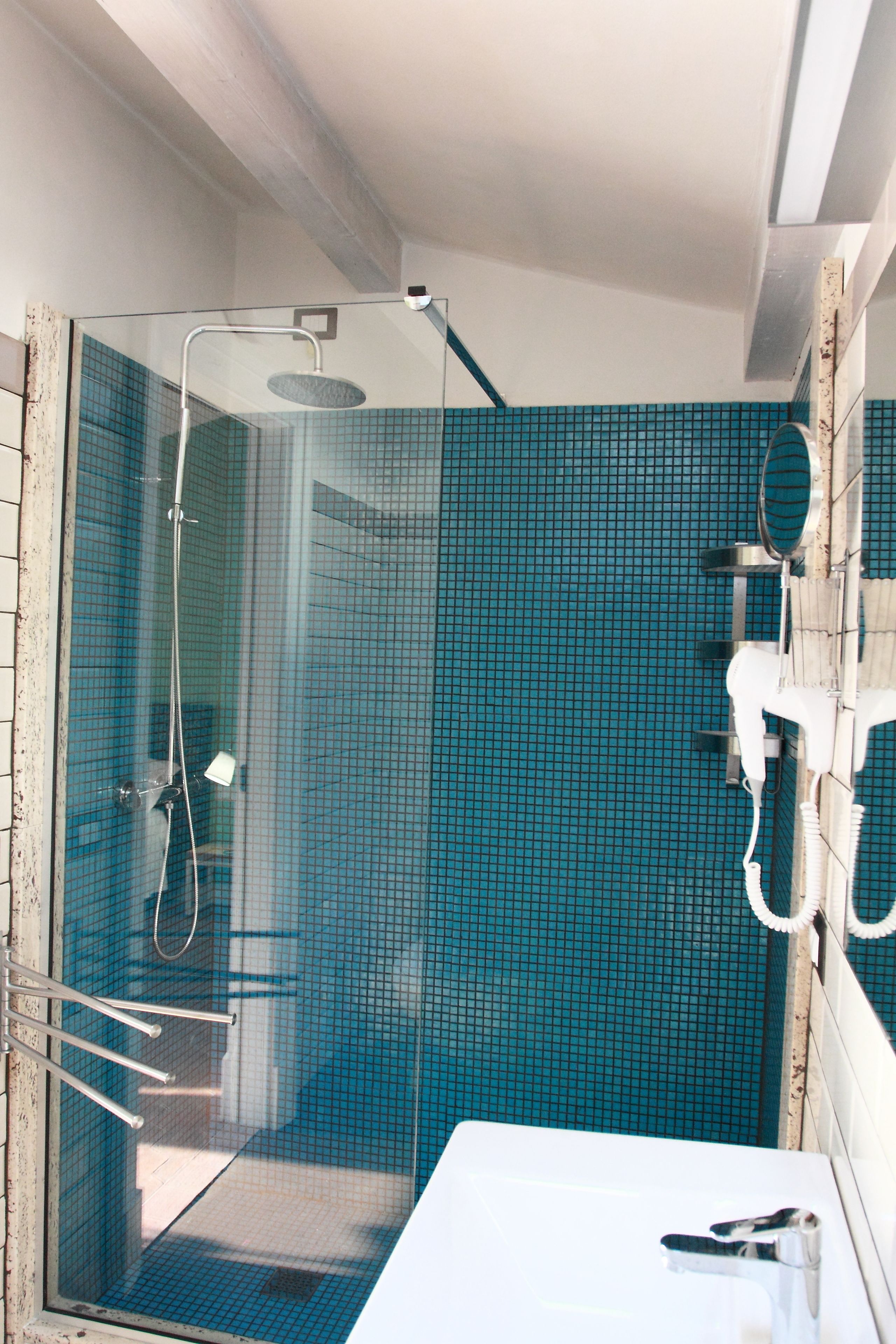 A shower with a glass door, a white sink, and a blue tiled wall.