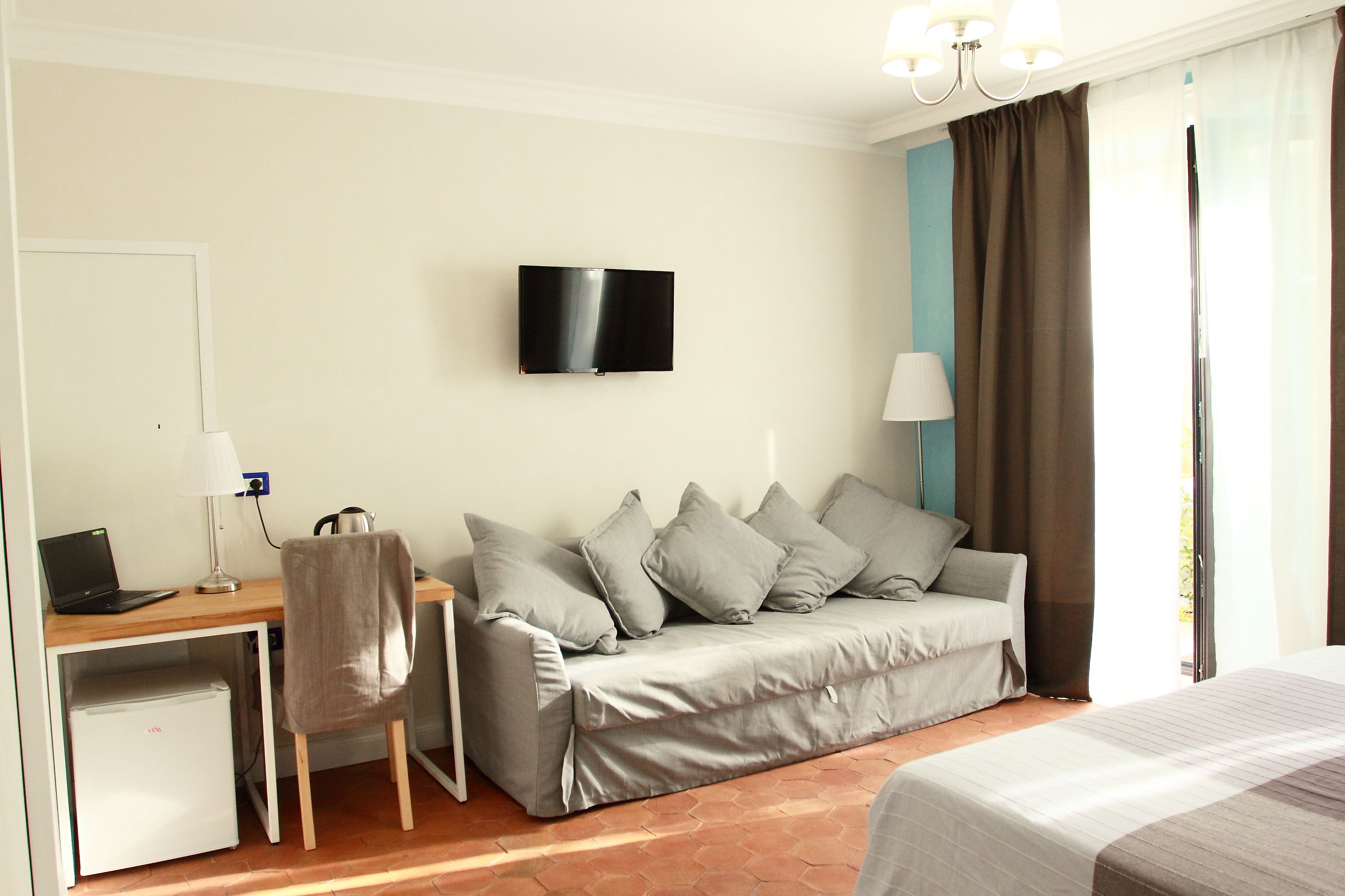 A hotel room with a bed, a desk with a laptop, a TV, a sofa, and a chair.