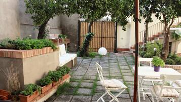Un patio con una mesa y sillas blancas, rodeado de plantas en macetas y una valla de bambú.