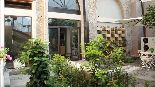 A stone building with a large arched window, outdoor seating area, and potted plants. - La Corte dei Limoni (Acireale)