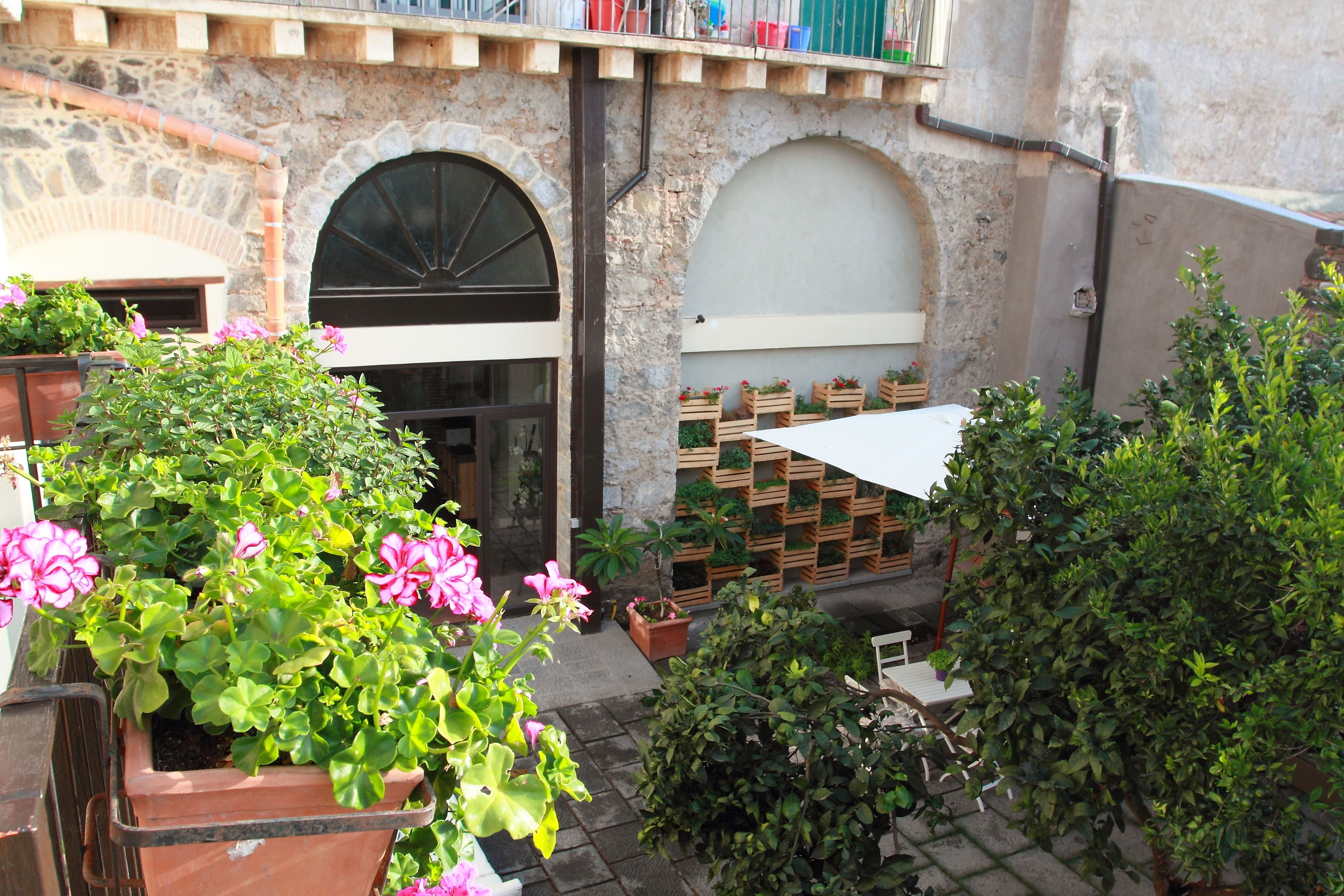 Un cortile con muro in pietra, fioriere di legno e un ombrellone bianco.