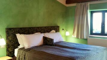 Una habitación con cama, mesita de noche, ventana con cortinas y lámpara de pared.
