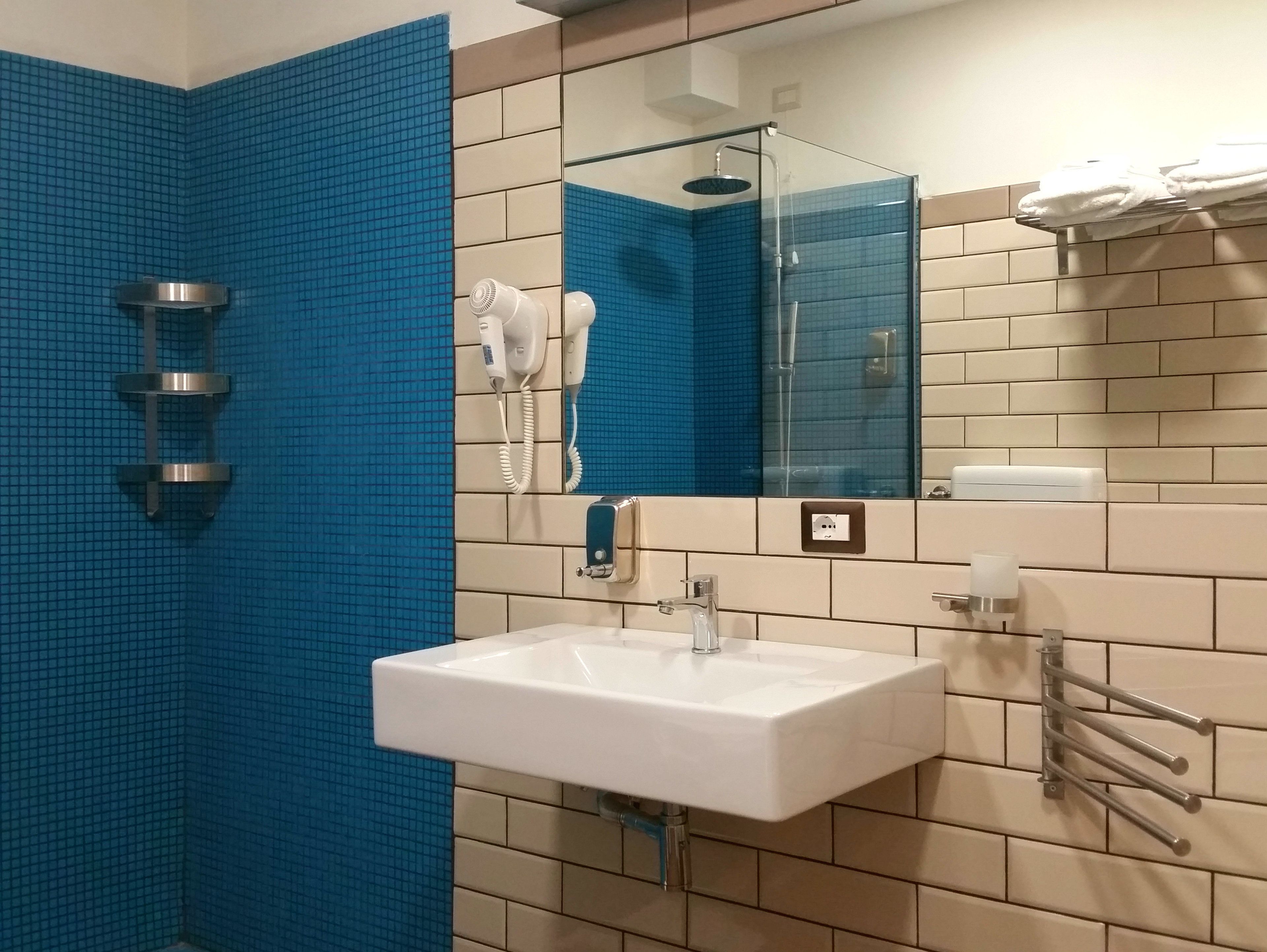 A bathroom with a blue-tiled shower wall, a white sink with a mirror above it, and a towel rack with folded towels.