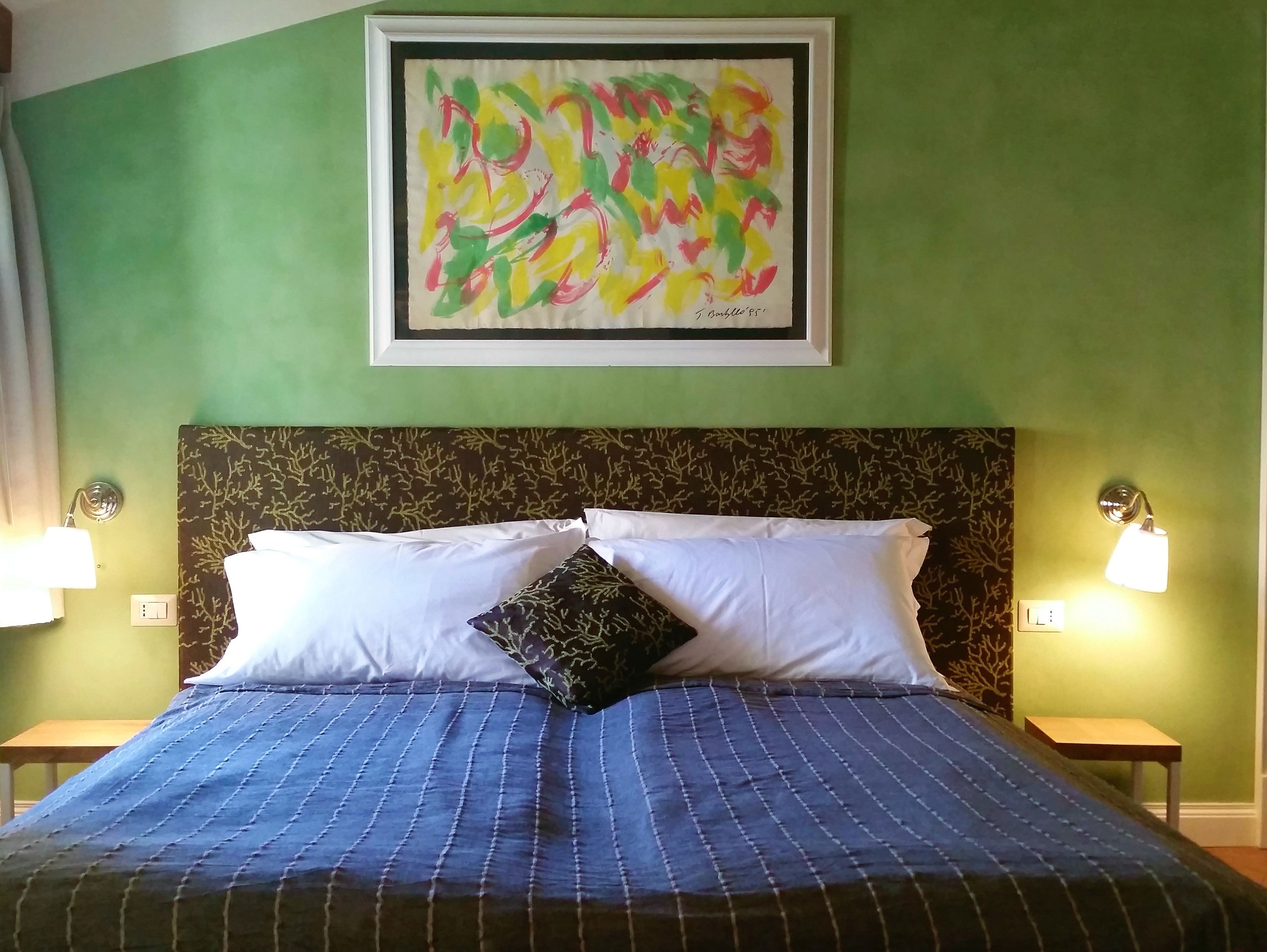 A hotel room with a bed, green walls, a framed abstract painting, and two bedside lamps.