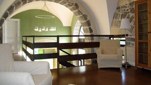 A room with a stone archway, a wooden bed frame, a white chair, a floor lamp, and a hanging light fixture. - La Corte dei Limoni (Acireale)