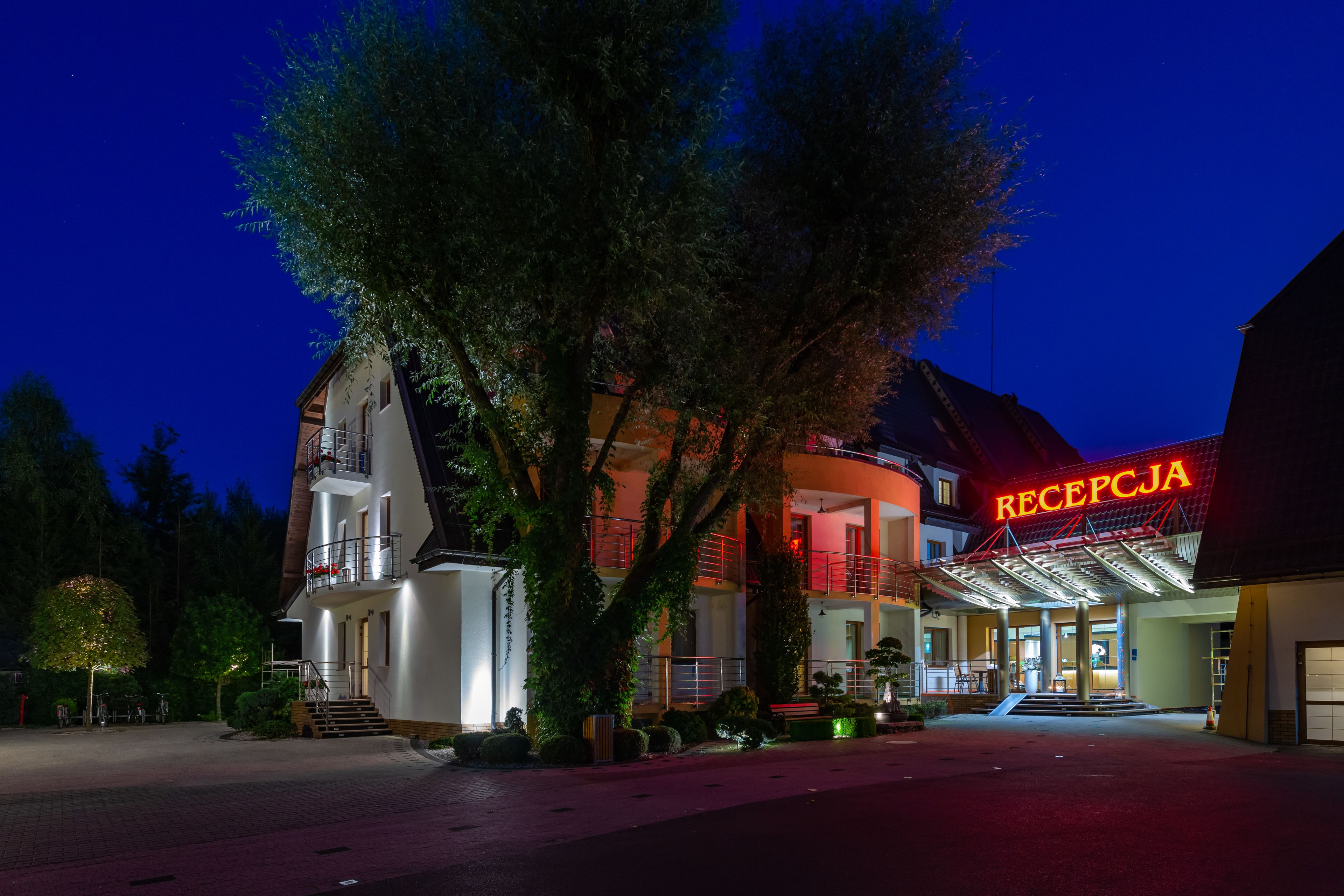 A hotel with a reception area, multiple floors, and a large tree in front.
