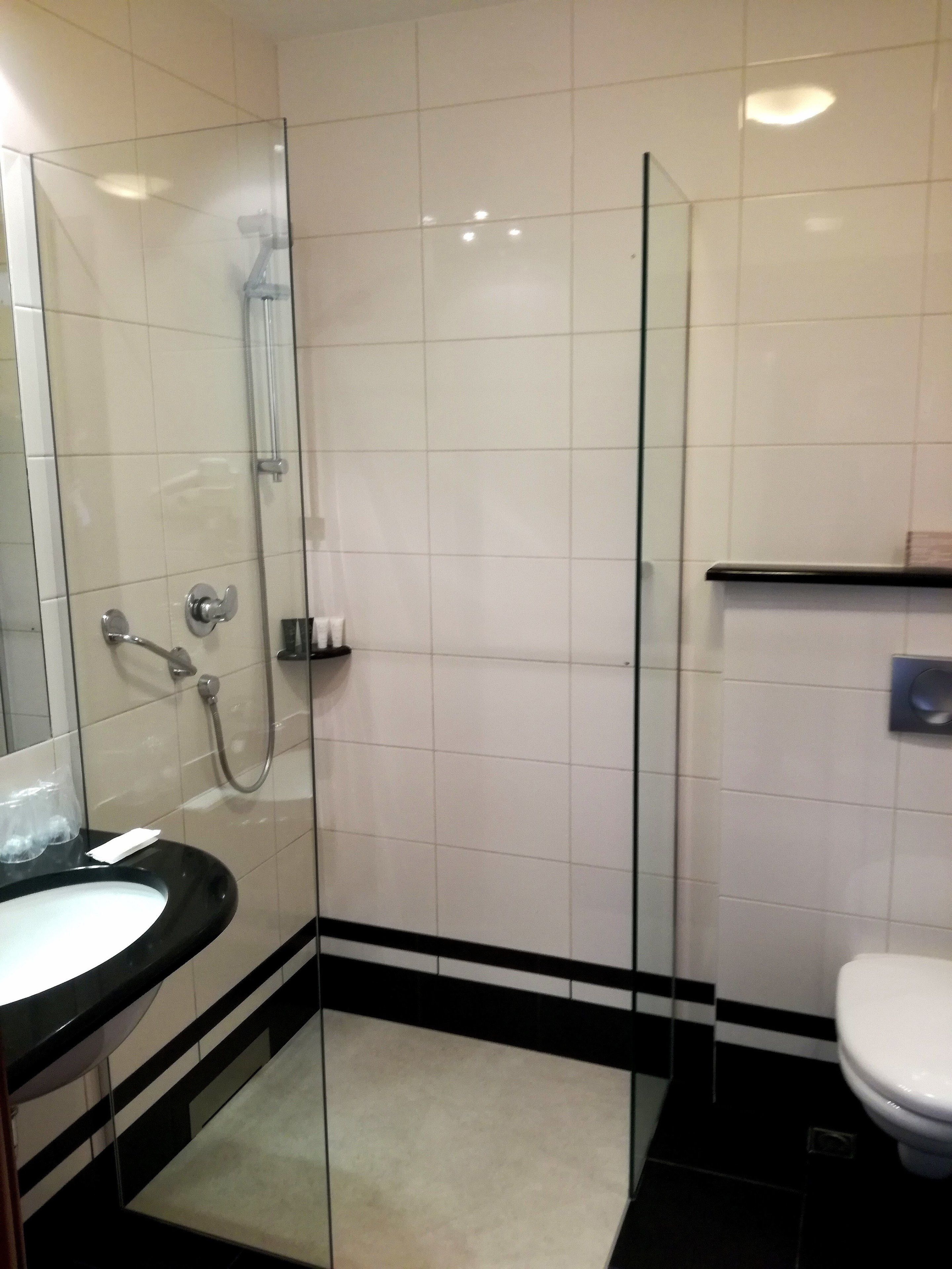Un baño moderno con ducha de vidrio, lavamanos negro y inodoro blanco.