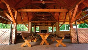 A covered picnic area with wooden benches and a central table, surrounded by brick walls and a brick fireplace. - Hotel Na Półboru (Sieradz)