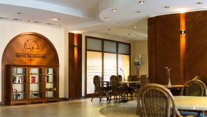 A hotel lobby with a wooden reception desk, a seating area with wicker chairs, and a large window with a view. - Hotel Na Półboru (Sieradz)