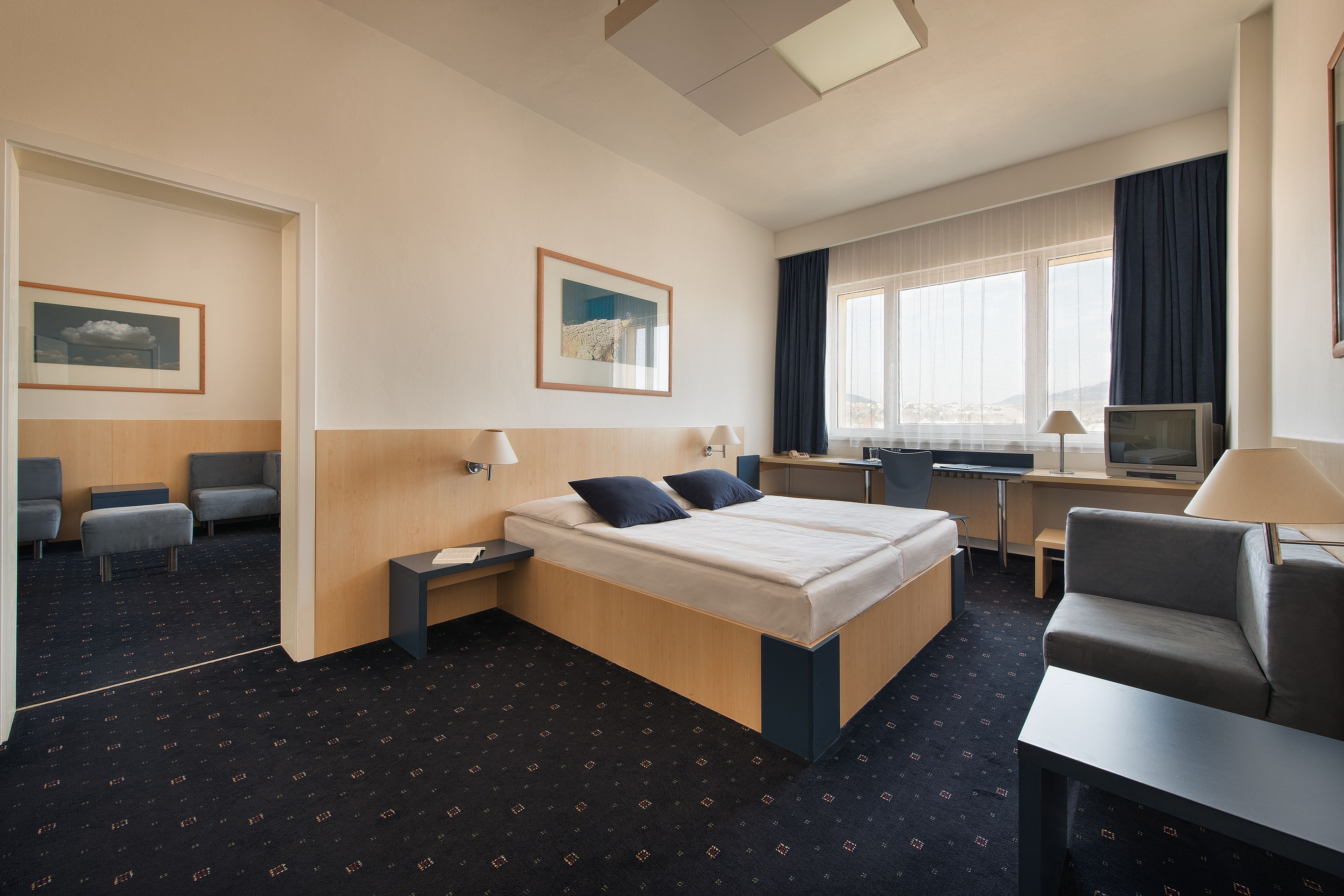 Habitación de hotel con cama, escritorio, silla, televisor y ventana con cortinas.