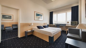 Habitación de hotel con cama, escritorio, silla, televisor y ventana con cortinas.