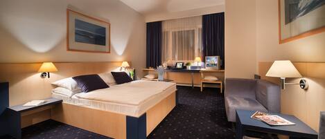 A hotel room with a bed, desk, chair, and a view of the city through the window.