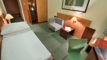 Habitación de hotel con cama, escritorio con computadora portátil, silla, mesita de noche con lámpara y armario.